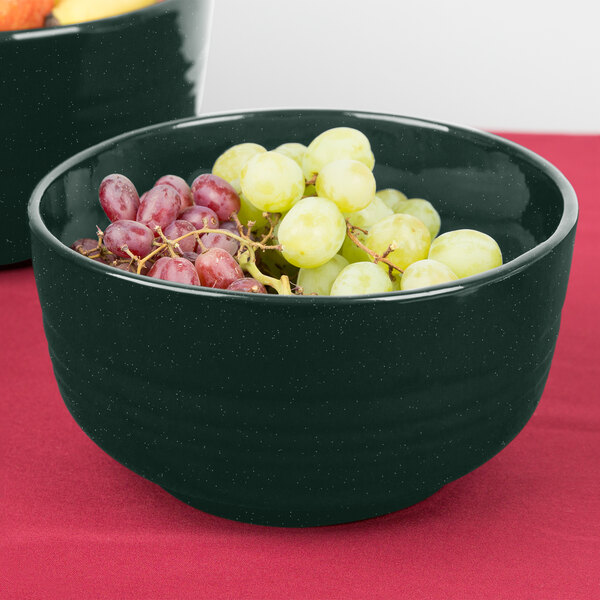 A Tablecraft hunter green and white speckled fruit bowl filled with grapes on a table.