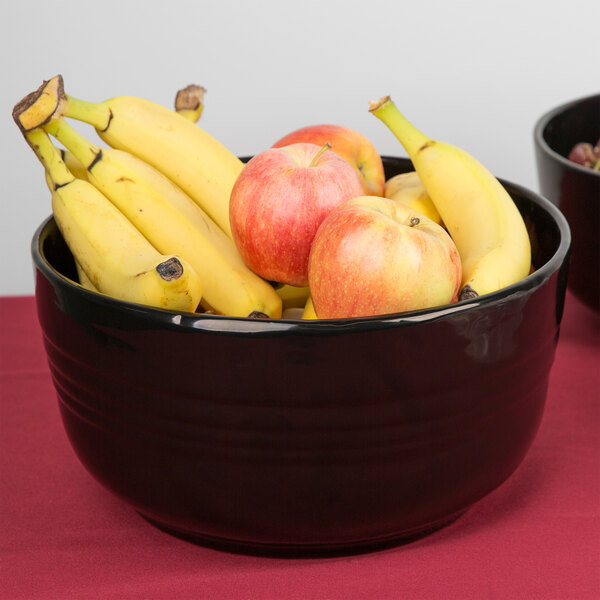 A Tablecraft black cast aluminum bowl filled with bananas and apples on a table.