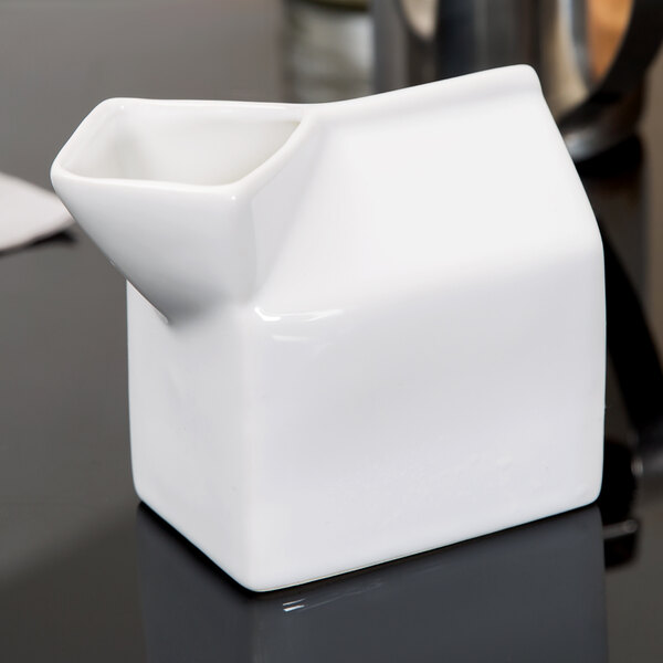 An American Metalcraft white ceramic milk carton creamer on a black surface.