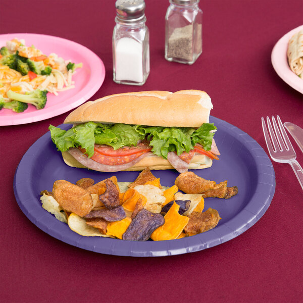 A sandwich with lettuce, tomato, and meat on a purple paper plate.