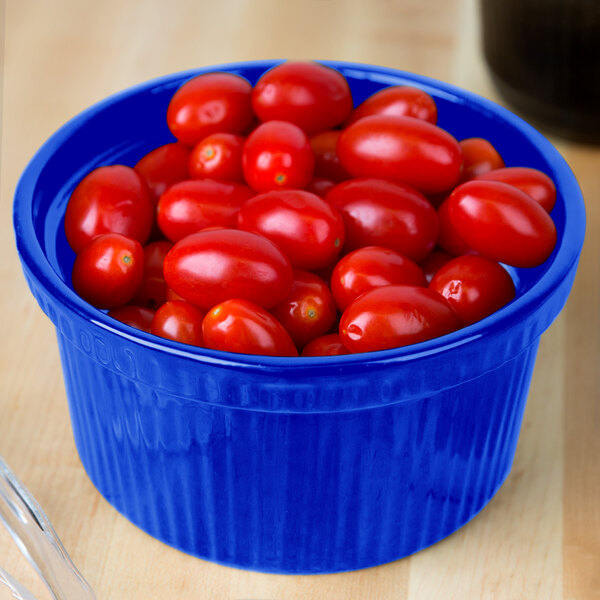 A blurry close up of a Tablecraft cobalt blue cast aluminum bowl with ridges filled with cherry tomatoes.