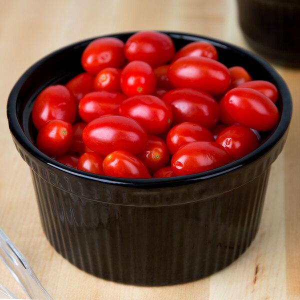 A Tablecraft black cast aluminum souffle bowl filled with cherry tomatoes on a table.