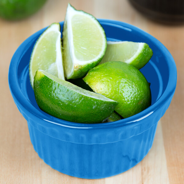 A Tablecraft sky blue cast aluminum bowl filled with limes on a counter.