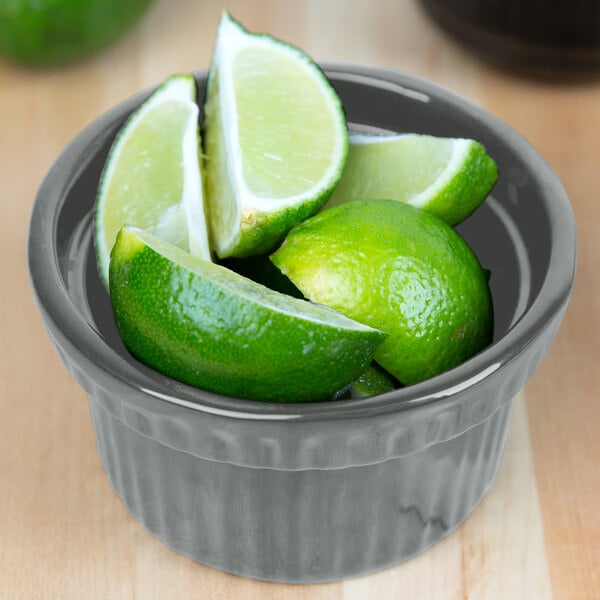 A Tablecraft gray cast aluminum souffle bowl filled with lime slices on a counter.