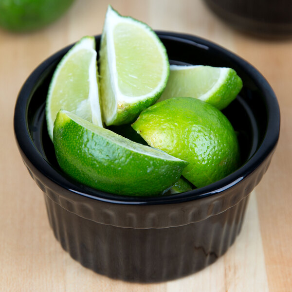 A Tablecraft black cast aluminum souffle bowl filled with lime wedges.