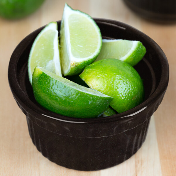 A Tablecraft black cast aluminum bowl with limes and lime wedges inside.
