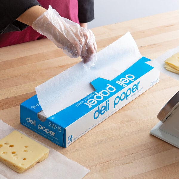 A person using Durable Packaging Interfolded Deli Wrap Wax Paper to wrap cheese on a metal surface.