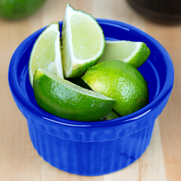 A Tablecraft cobalt blue cast aluminum bowl filled with limes and lime wedges.