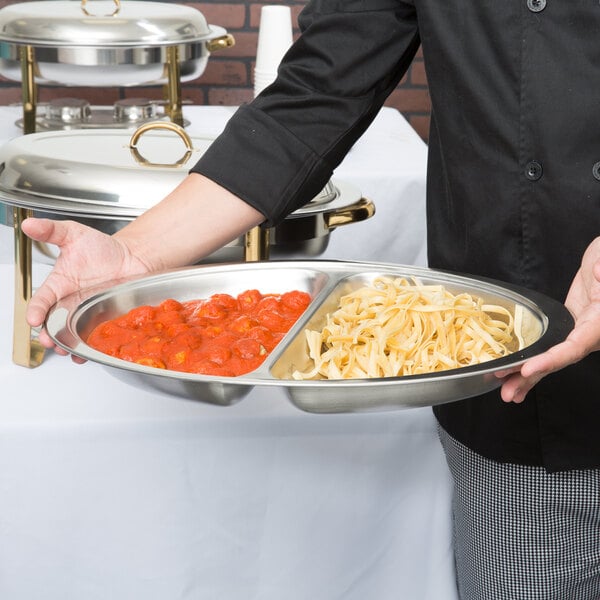 A person holding a silver tray with a Choice Deluxe Divided Food Pan filled with pasta and sauce.