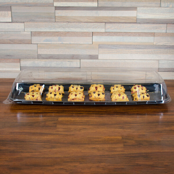 A Sabert clear plastic catering tray with a high dome lid on a table with a tray of pastries.