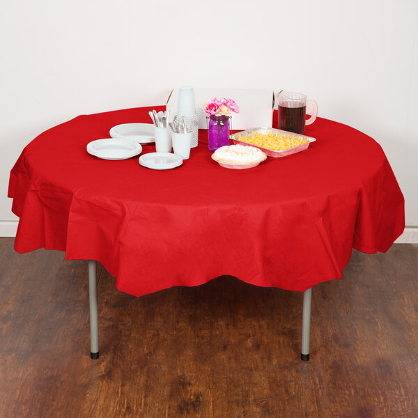 A table with a red Creative Converting Classic Red OctyRound table cover, plates, and cups on it.
