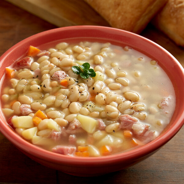 A bowl of soup with navy beans, ham, and vegetables.