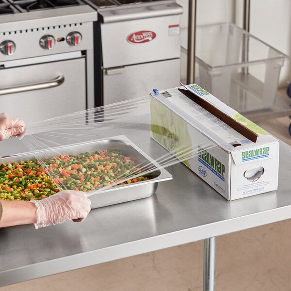 A person using plastic gloves to wrap a tray of vegetables in Berry Heavy-Duty Film.