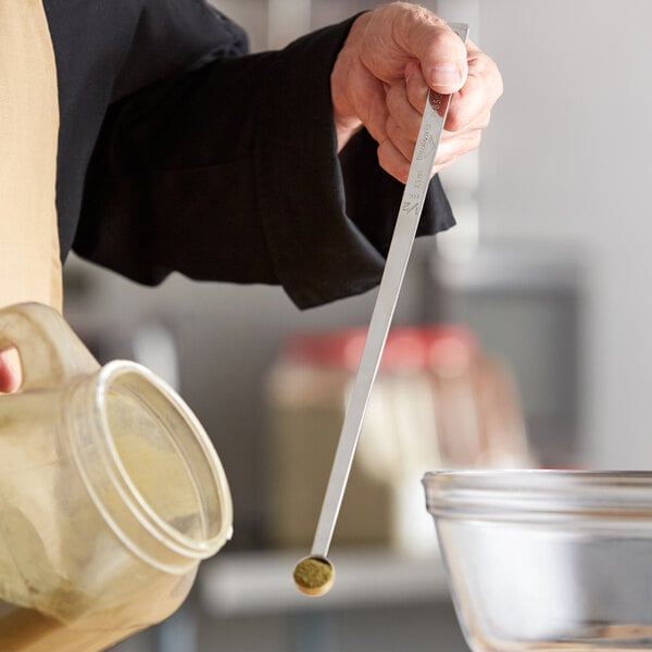 A person using a Vollrath long handled measuring spoon to measure ingredients in a glass bowl.