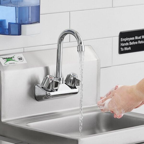 A person washing their hands under a Regency wall mount faucet with a swivel gooseneck spout.