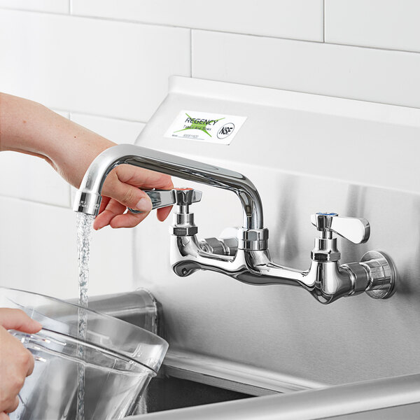 A person's hand pouring water from a Regency wall mount faucet.