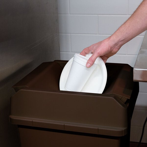 A hand putting a white cup in a brown Continental lid on a trash can.