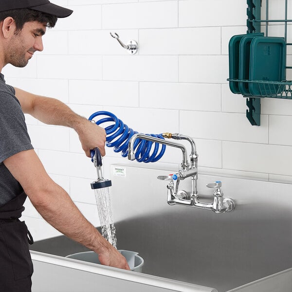 A man using a T&amp;S wall mount pet grooming faucet to fill a sink using a hose.