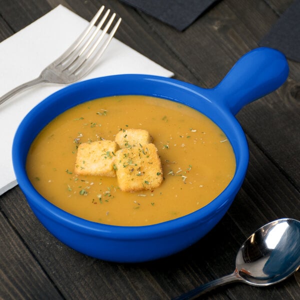 A Tablecraft cobalt blue cast aluminum soup bowl with a bowl of soup with a spoon and fork.