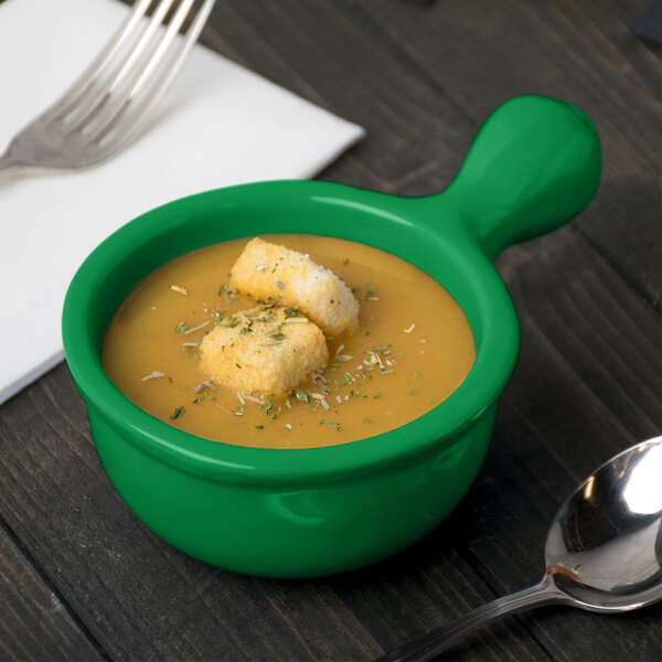 A green cast aluminum soup bowl with croutons on top next to a spoon and fork.