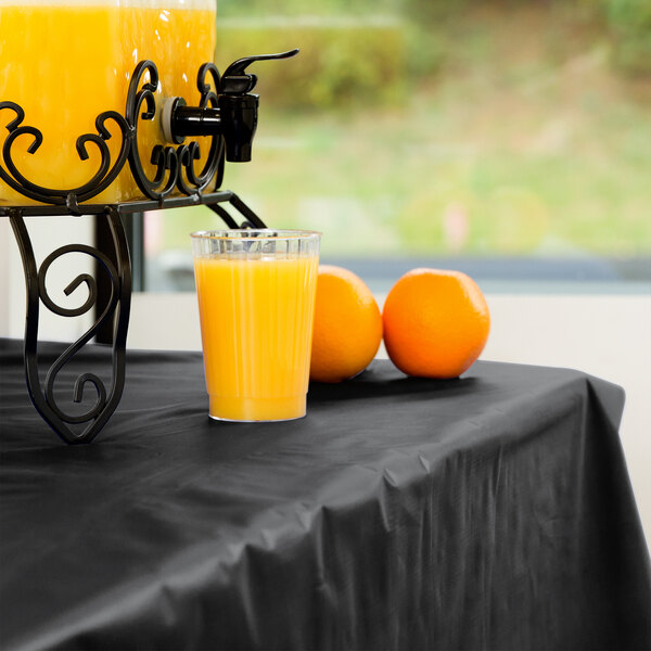 A black plastic table covered with a glass of orange juice and two oranges.
