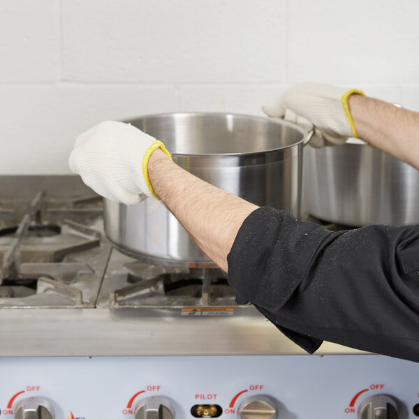 A person wearing Cordova seamless loop in terry gloves holds a pot on a stove in a professional kitchen.