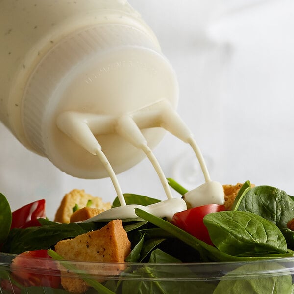 A salad being poured into a bowl using a Vollrath Tri Tip bottle cap.