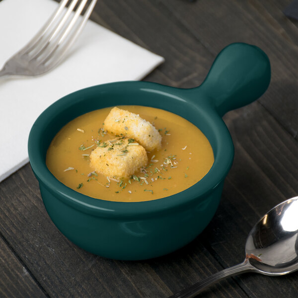 A Tablecraft hunter green cast aluminum soup bowl with croutons and a spoon on a table.