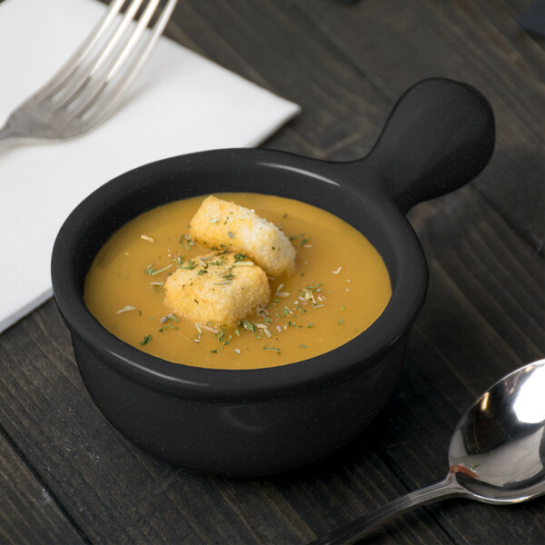 A Tablecraft black cast aluminum soup bowl with croutons on top and a spoon.