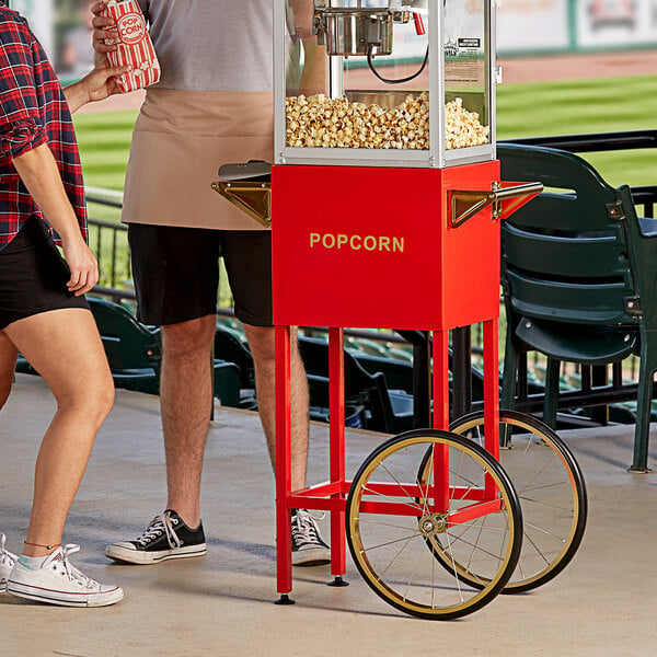 A tan aproned person standing next to a Carnival King popcorn cart filled with popcorn.