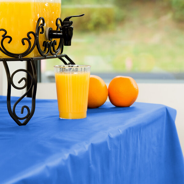 A table with a blue Atlantis Plastics table cover and a glass of orange juice on it.