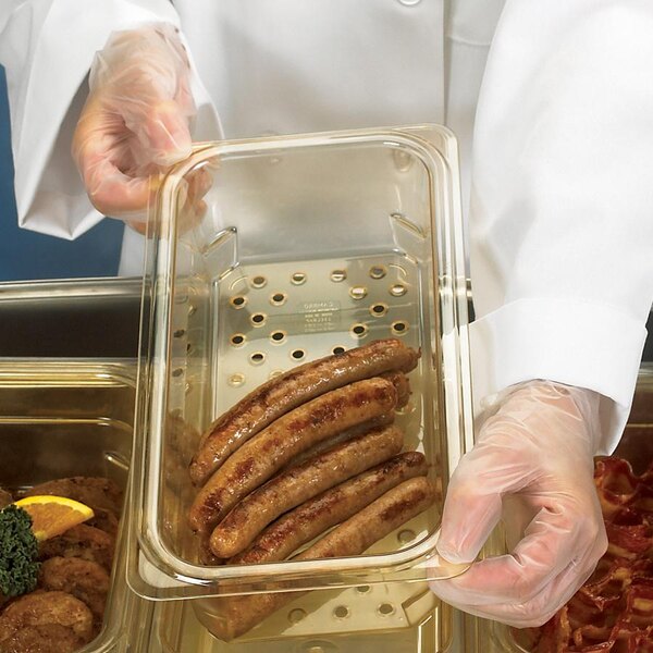 A gloved hand using a Cambro amber plastic colander pan to hold sausages.