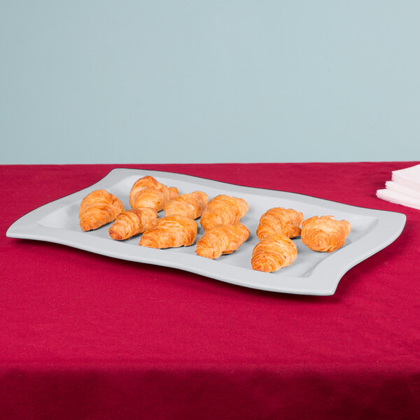 A natural cast aluminum rectangular platter with croissants on a table.