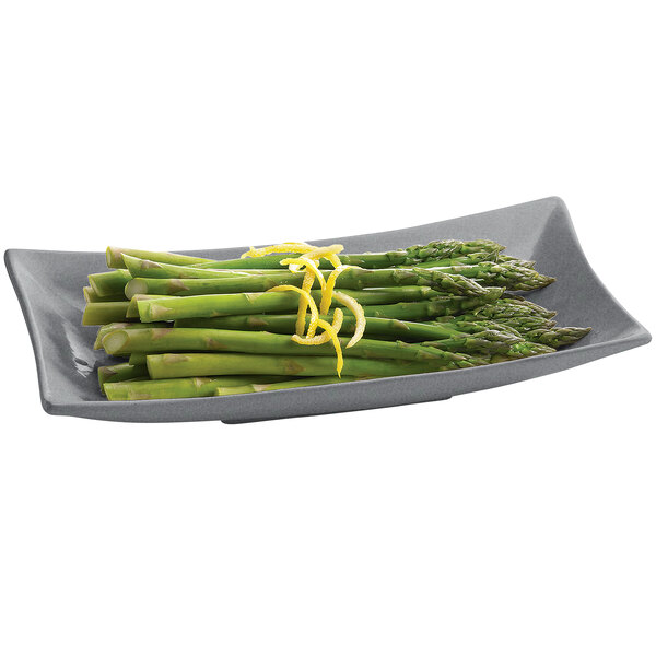 A Tablecraft granite flared rectangle platter with asparagus and lemon zest on it.