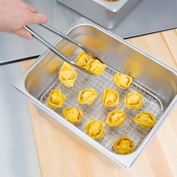 A hand using tongs to remove yellow food from a Vollrath stainless steel rack.
