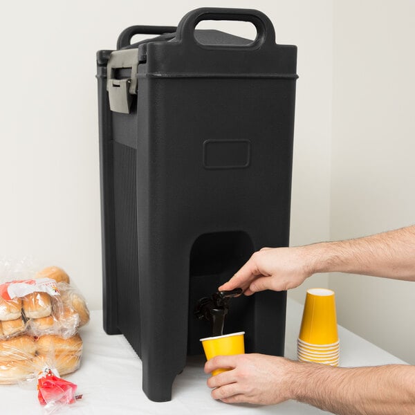 A man pouring coffee into a Carlisle black insulated beverage dispenser.