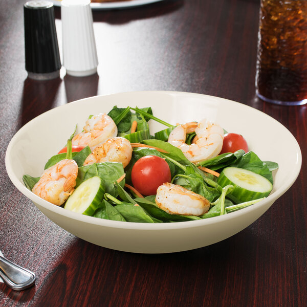 A Diamond Ivory melamine bowl filled with salad on a table.