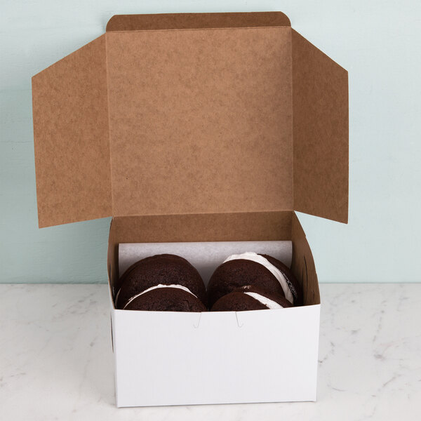 A 7" x 7" x 4" white bakery box with the lid open and three chocolate donuts inside.