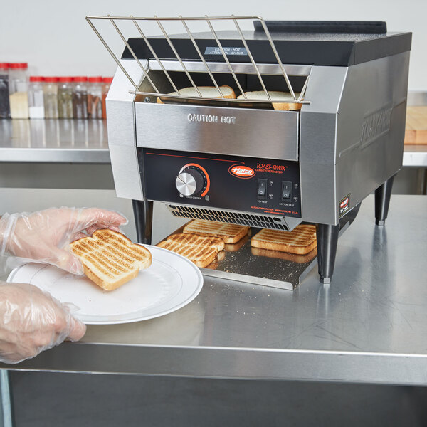 A person in gloves holding a plate with toast from a Hatco TQ-10 Conveyor Toaster.