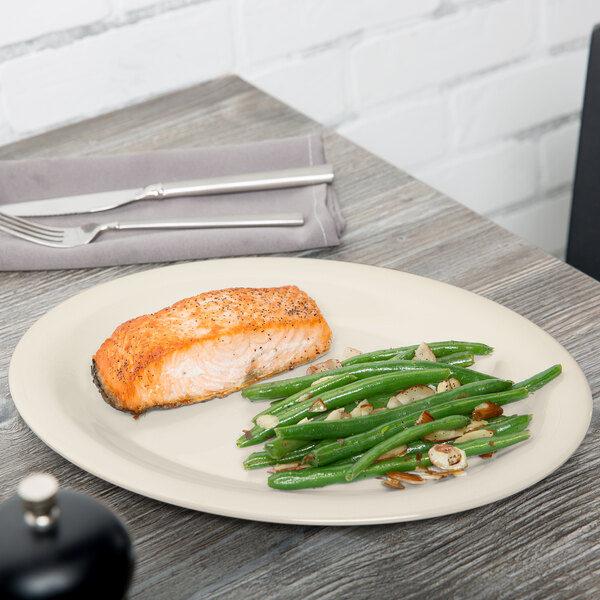 An ivory oval platter with salmon and green beans on a table.