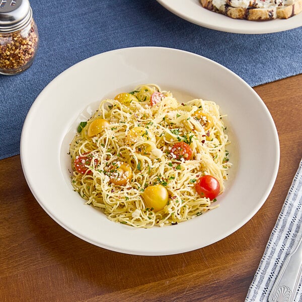 An Acopa ivory stoneware bowl filled with pasta, tomatoes, and cheese.