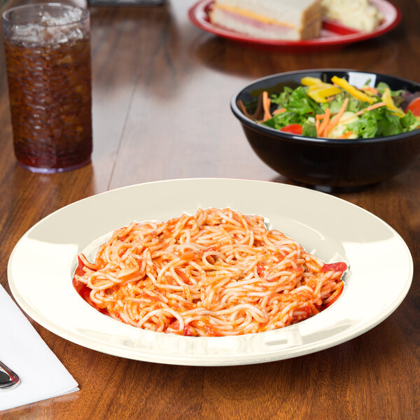 A bowl of salad with vegetables and a plate of spaghetti with sauce on a table.