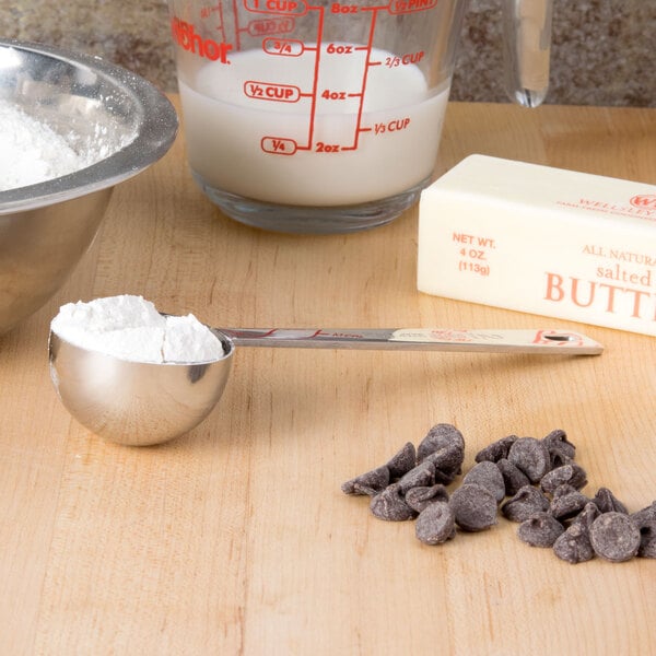 A Tablecraft stainless steel coffee measuring spoon with flour and chocolate chips on a table.