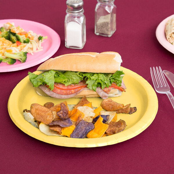 A sandwich on a Creative Converting Mimosa Yellow paper plate on a table.