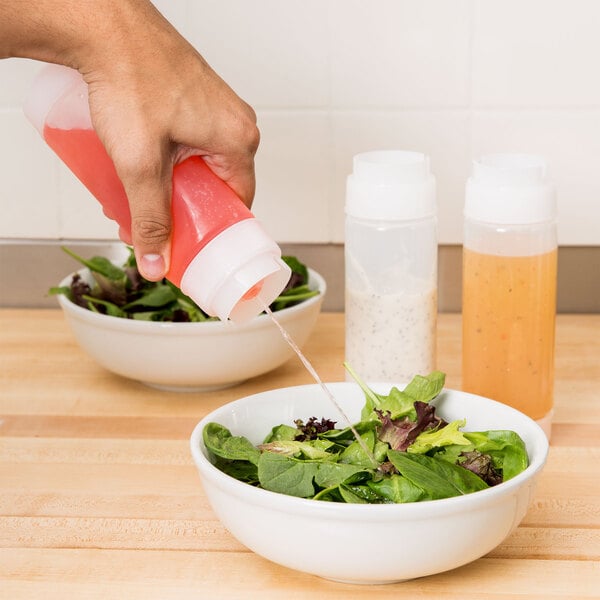 A hand squeezing Tablecraft Dualway Squeeze Bottle to pour pink liquid onto a bowl of salad.