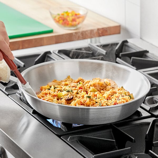 A person cooking food in a Choice aluminum fry pan on a stove.