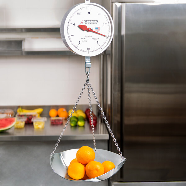 A Cardinal Detecto hanging scoop scale with a bowl of oranges on it.