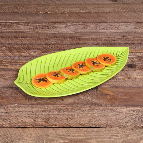 An Elite Global Solutions green melamine platter with a leaf shaped like a banana holding sliced fruit on a wood surface.
