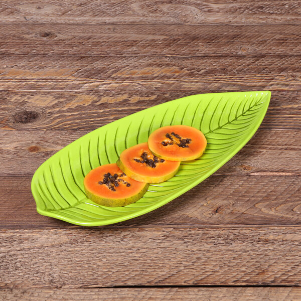 A green leaf-shaped Elite Global Solutions melamine plate with sliced fruit on it.