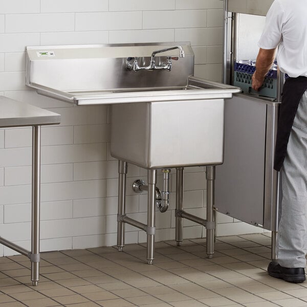 A man standing in a commercial kitchen with a Regency stainless steel sink on a counter.
